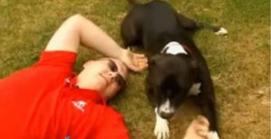 Foto de um homem deitado na grama com seu cão ao lado