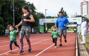 Foto de menina com mão dada com a mãe e outra de mão dada com o pai na pista de atletismo do Bolão 