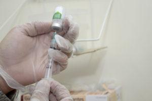 Mãos com luvas higiênicas segurando seringa e frasco de vacina contra gripe