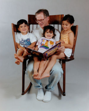 Pai lendo sentado na cadeira para os três filhos 