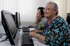 Duas mulheres idosas, em frente a computadores