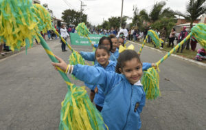 Crianças na rua carregando balizas decoradas com fitas