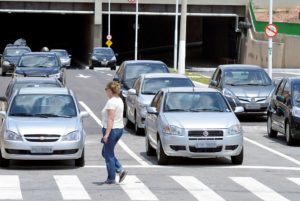 Mulher atravessando na faixa da pedestre em frente a carros parados
