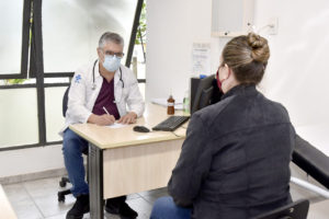 Medico sentado em frente de mulher paciente e fazendo anotações