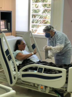 Mulher em leito de hospital olha para dispositivo eletrônico segurado por enfermeira